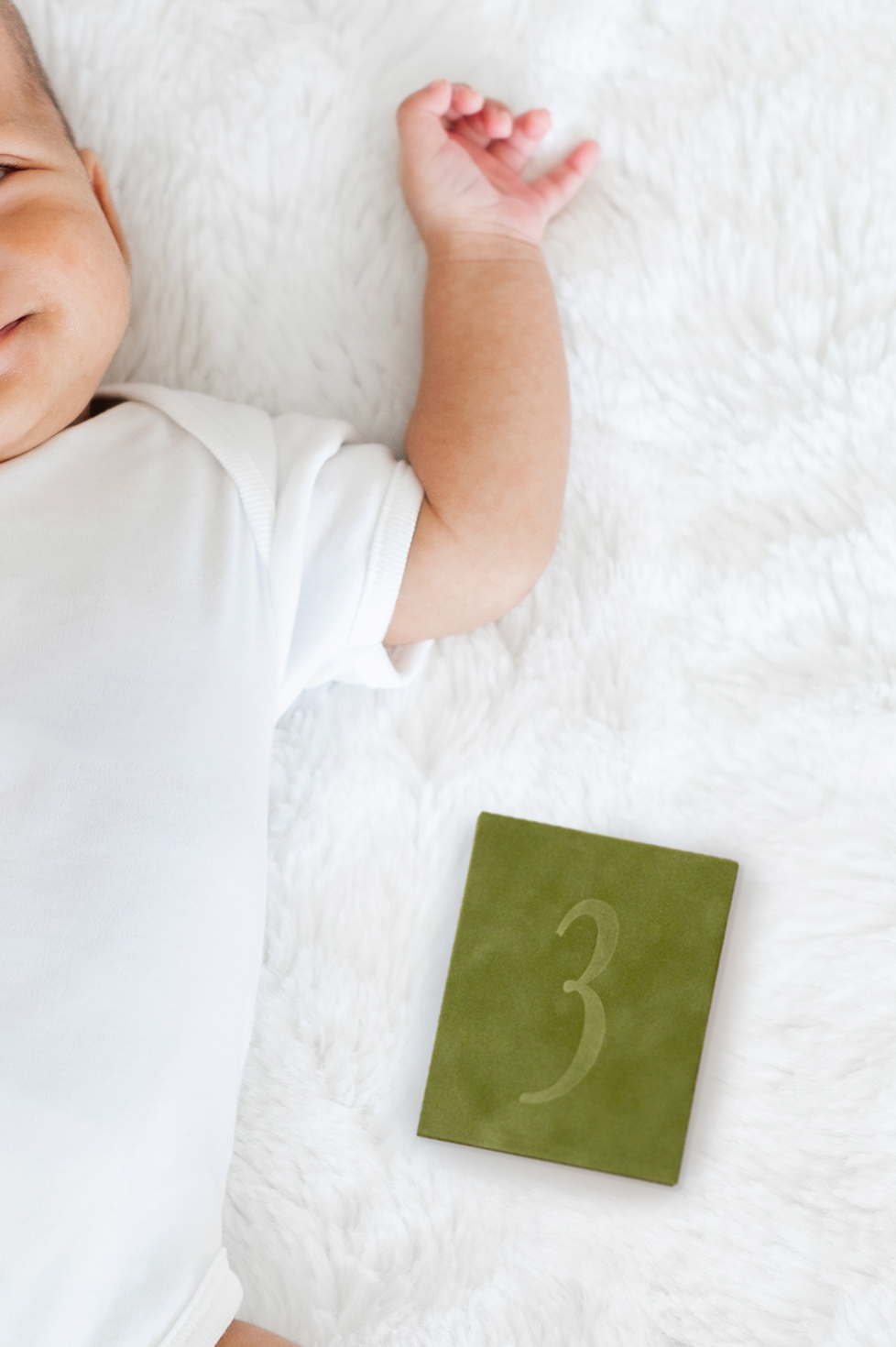 Baby's arm with a green card displaying the number 3 on a white blanket